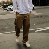 Man in a white shirt and brown pants standing on a city street.